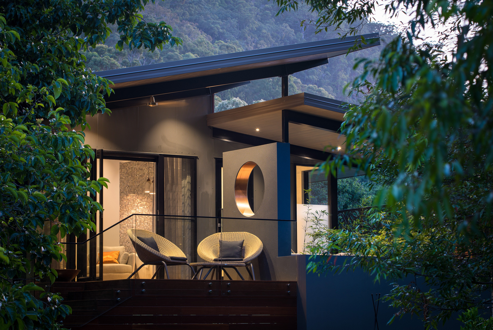 A person rests peacefully in a green hammock surrounded by lush forest trees, wearing headphones and looking serene. The scene captures a moment of tranquil relaxation in a natural woodland setting.