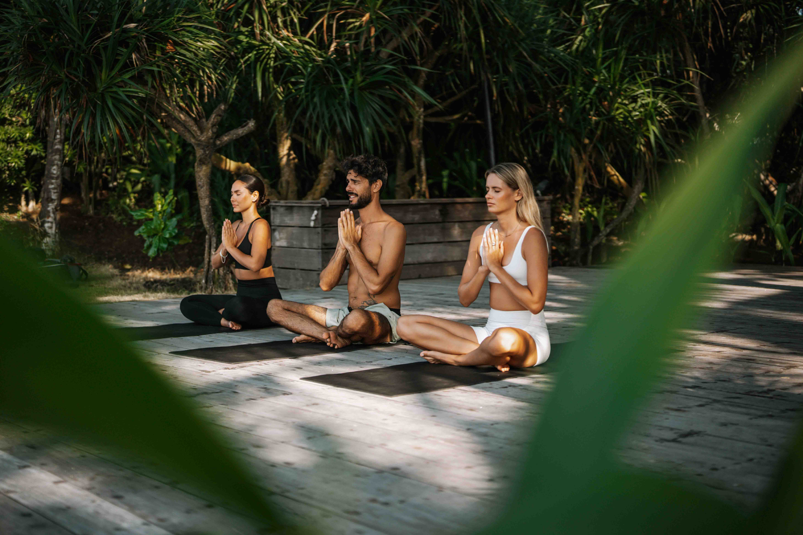 KOMUNE_IMG3-24 A serene outdoor massage treatment on a wooden deck surrounded by lush tropical forest, with a massage therapist providing a relaxing massage to a client.