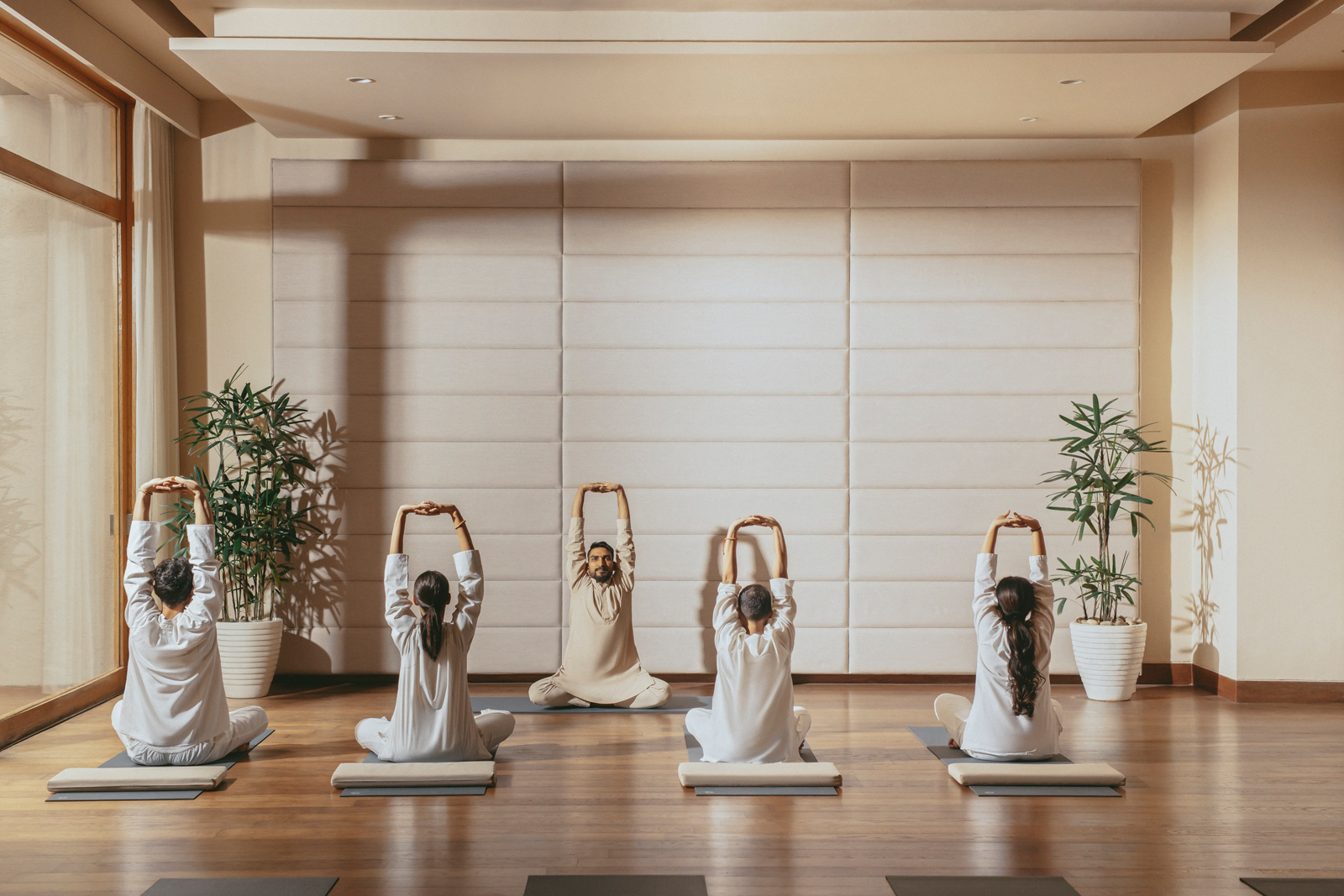 An open-air wooden dining area with traditional architectural design, featuring a large communal table set for a meal, surrounded by wooden columns and offering panoramic views of a green tropical landscape.